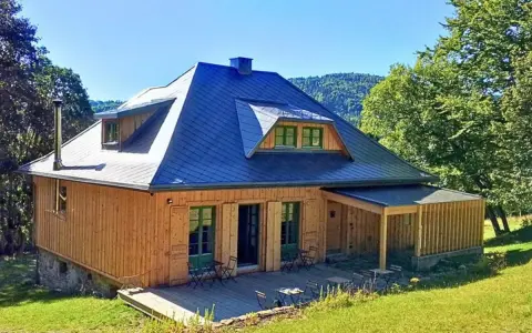 Drewniany domek z niebieskim dachem, tarasem i zielonymi okiennicami. Idealne schronisko oźna na górskim stoku.