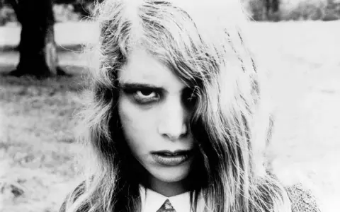 Primo piano di una bambina con sguardo inquietante, capelli lunghi e spettinati. Un'immagine iconica per chi ama i film trash da vedere.