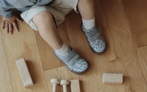 Roczne dziecko bawi się klockami na drewnianej podłodze. Ma na sobie buty z kotkami, idealne do chodzenia po domu.