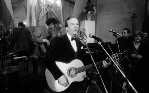 Zbigniew Kurtycz z gitarą i zespołem wykonuje swoje utwory. Wokalista w czarnym aksamitnym fraku śpiewa do mikrofonu.