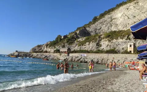 Persone si godono una giornata di sole sulla spiaggia di Erchie, con il mare azzurro e una scogliera imponente alle spalle.