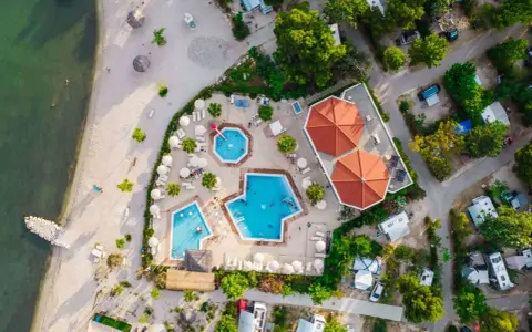 Widok z lotu ptaka na kemping z basenami i plażą. Widać tu podział na strefy: plażową, basenową i kempingową z kamperami.