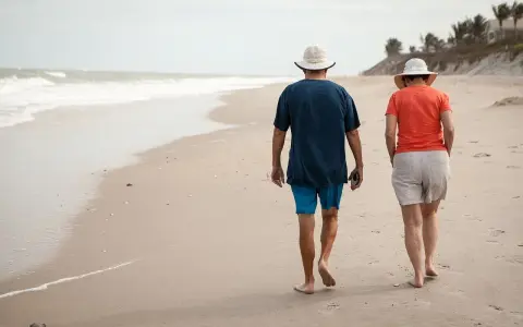Spacerem po plaży idą emeryci. Słońce, morze i piasek tworzą idealne tło dla ich wspólnego wypoczynku.