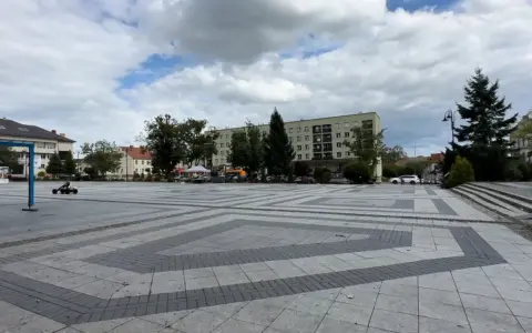 Dziecko na gokarcie przemierza pusty plac, który może być największym rynkiem w Polsce. W tle budynki mieszkalne i drzewa.