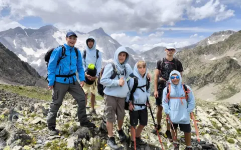 Groupe d'enfants et d'un adulte en randonnée en montagne, souriants, avec des sacs à dos et des bâtons de marche.