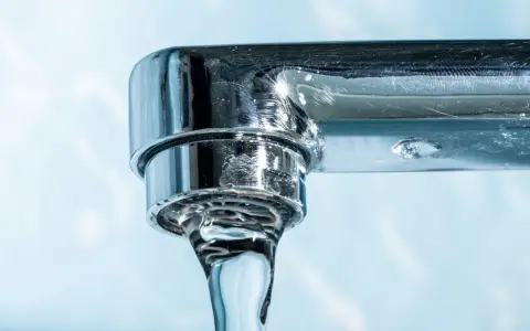 Gouttes d'eau tombant d'un robinet chromé, montrant des dépôts calcaires, un signe du tableau dureté de l'eau.