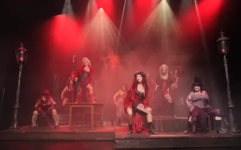 Scena z musicalu "Les Miserables" z kobietami w strojach z epoki, w czerwonym świetle i dymie.
