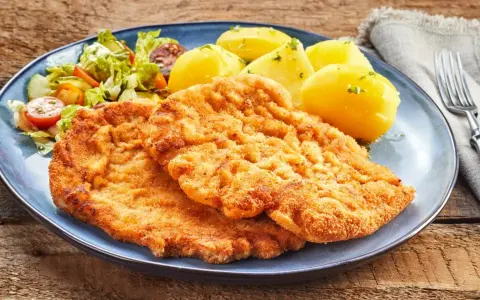 Dwa chrupiące kotlety, jeden sznycel cielęcy, drugi kotlet schabowy, podane z ziemniakami i sałatką.