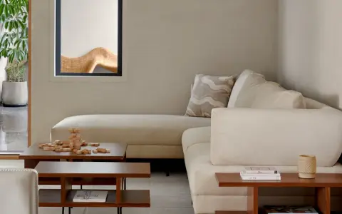 Sofá modular beige, mesa de centro de madera con juego de Jenga, planta en maceta y ventana con detalle decorativo. Ambiente de estilo cozy.