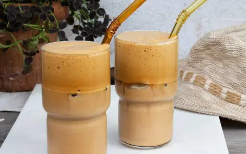 Två glas med iskaffe, perfekt för ett somrigt iskaffe recept. Med tjockt skum och isbitar.