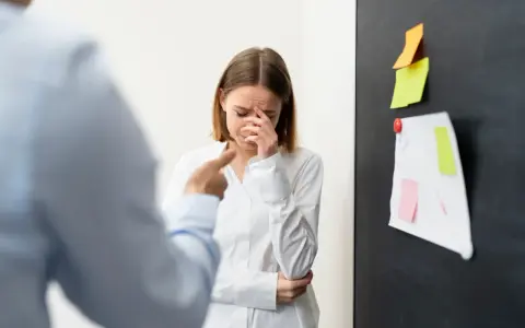 Mujer llora mientras un colega la señala, sufriendo acoso laboral.