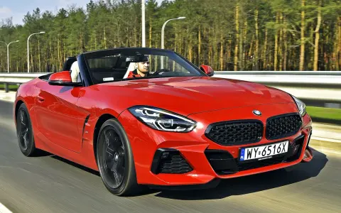 Czerwone z4 bmw z opuszczonym dachem pędzi po drodze, kierowca w czapce z daszkiem cieszy się jazdą.