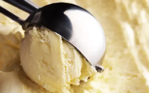 Un cucchiaio raccoglie una pallina di cremoso gelato con yogurt greco, pronto per essere gustato.
