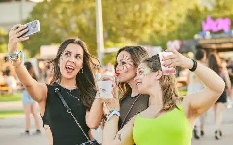 Tres amigas con maquillaje festivo y bebidas en un festival de verano.