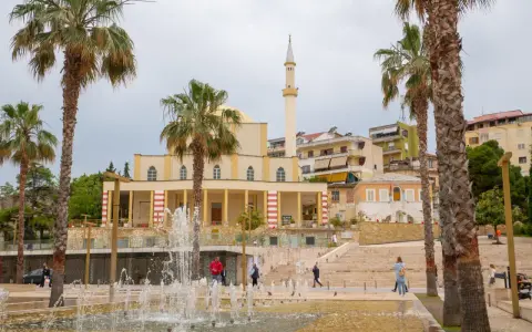 Plac z fontannami i palmami przed meczetem w Durrës, Albania. Ludzie spacerują po schodach.