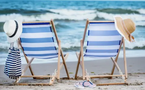 Dwa leżaki z niebiesko-białymi pasami, plażowe kapelusze i torba. Idealne miejsce na sea camp.