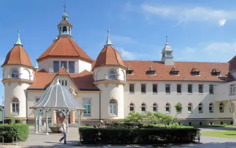 Elegancki zakład balneologiczny Sopot z charakterystycznymi wieżyczkami i czerwonym dachem, otoczony zielenią.