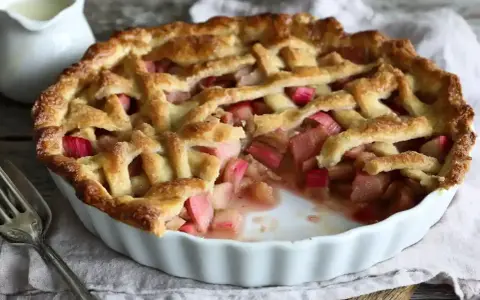 Gyllene rabarberpaj med flätat lock, perfekt för ett somrigt rabarber recept. En bit saknas, redo att avnjutas.