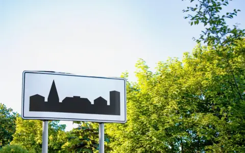 Znak informuje o wjeździe do obszaru zabudowanego. Sylwetka miasta na białym tle.