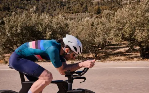 Cyclist pushing hard on a road bike, focused on a VO2 max workout amidst a scenic, tree-lined landscape.