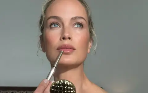 Kobieta z błękitnymi oczami precyzyjnie wykonuje makijaż wieczorowy, podkreślając usta konturówką.