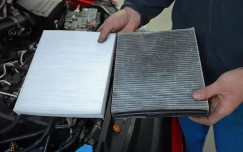 Hands hold a new white air filter next to a dirty, used one, ready to replace air filter in car.