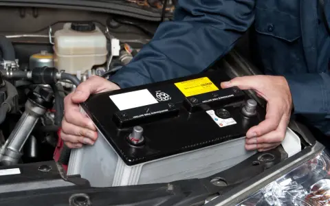 Personen håller i ett bilbatteri för att koppla in det i bilen.