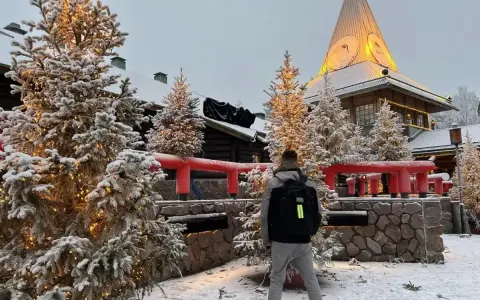 Ośnieżone choinki i budynek z wieżą w Rovaniemi, gdzie mieszka mikołaj. Mężczyzna z plecakiem stoi tyłem.