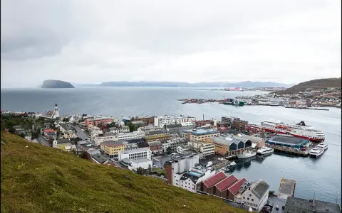 Vy över en stad vid havet med färjor vid kaj. En kyrka med högt torn syns i förgrunden. Detta är Norges nordligaste stad.