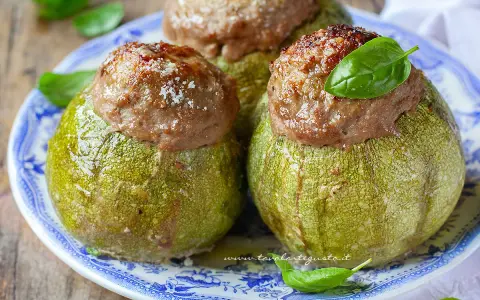 Zucchine tonde ripiene, un piatto gustoso del menù di Benedetta, servite su un piatto blu e bianco con basilico fresco.