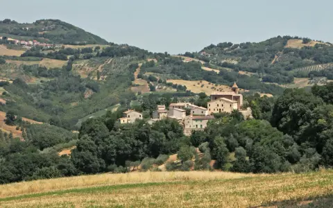 Borgo collinare di **Cerreto di Saludecio** con case in pietra e una chiesa, immerso nel verde della campagna romagnola.