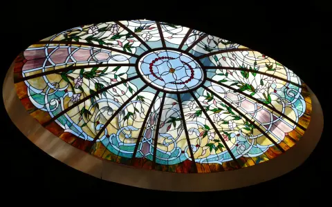 Magnifique vitrail intérieur maison, orné de fleurs roses et de motifs végétaux bleus et jaunes, illuminant la pièce.