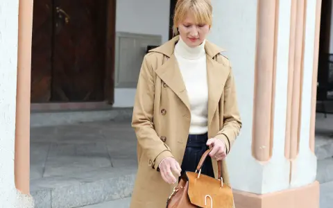 Kobieta w beżowym prochowcu i golfie, z brązową torebką, uosabia paryski styl ubierania.