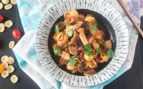 Orecchiette con pesce spada e melanzane, un piatto saporito e colorato, guarnito con basilico fresco.
