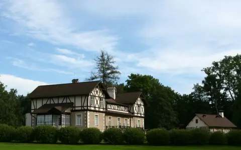 Elegancki dom z charakterystyczną konstrukcją szachulcową, otoczony zielenią, pod błękitnym niebem z chmurami.