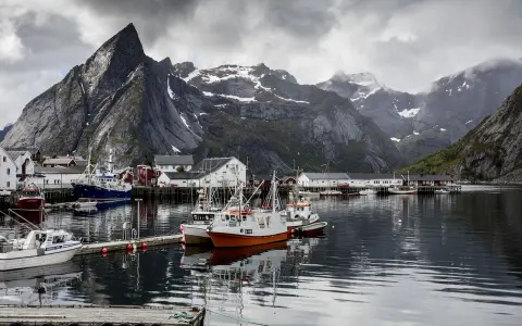 Port de pêche norvégien avec des montagnes imposantes en arrière-plan. Des bateaux de pêche sont amarrés, offrant un mouillage bateau gratuit dans ce paysage pittoresque.