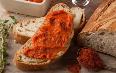 Fetta di pane con 'nduja, un assaggio di cosa mangiare in Calabria. Spezie rosse e pane fresco completano la scena.