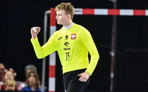 Marcel Jastrzębski, młody bramkarz w żółtej koszulce z orłem, zaciśniętą pięścią świętuje udaną interwencję.