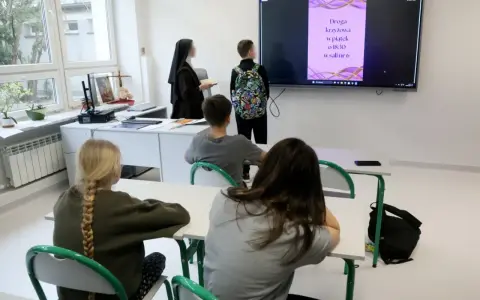Lekcja religii w szkole. Czy religia wlicza się do średniej? Nauczycielka w habicie i uczniowie patrzą na ekran z informacją o Drodze Krzyżowej.