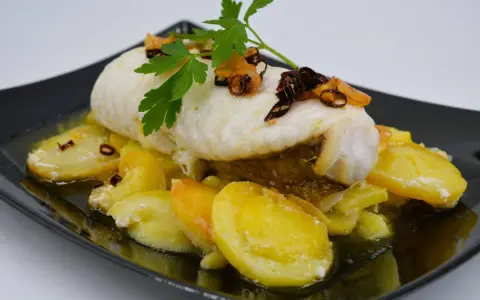 Rape con patatas, un plato delicioso con pescado blanco tierno y patatas doradas, decorado con perejil fresco y crujientes trozos de ajo frito.