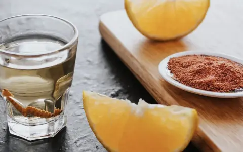 Ein Glas Tequila mit Wurm, daneben Orangenstücke und eine Schale mit Gewürzmischung.