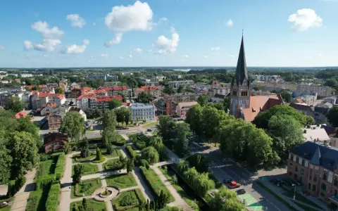 Widok z lotu ptaka na Szczecinek. Widać park miejski z fontanną, kościół z wieżą i zabudowania. To piękne **szczecinek atrakcje** turystyczne.