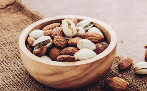Un bol en bois rempli d'amandes et de pistaches, une liste d'oléagineux parfaite pour une collation saine.