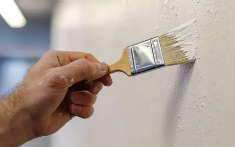Mano aplicando pintura blanca con brocha, creando texturas. Descubre trucos para pintar paredes con efectos únicos.