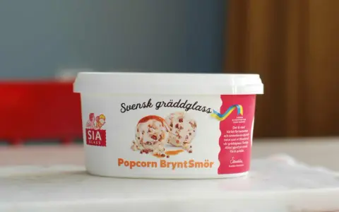 En burk SIA gräddglass med smak av popcorn och brynt smör. Glasskulor med kolasås och popcorn syns på etiketten.