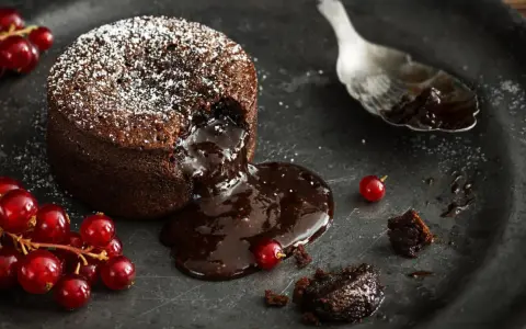 Schokoladen-Lava-Kuchen mit flüssigem Kern, bestäubt mit Puderzucker, garniert mit roten Johannisbeeren. Ein köstliches Lava Cake Rezept.