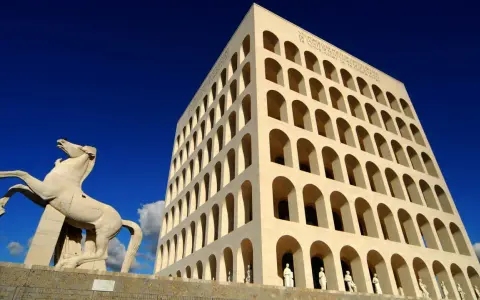 Le palais de la civilisation italienne, monument emblématique, se dresse fièrement sous un ciel bleu éclatant, avec une statue de cheval en avant-plan.