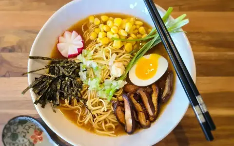 A miska pełna aromatycznego ramen miso z makaronem, jajkiem na pół, kukurydzą, grzybami shiitake, nori i szczypiorkiem.