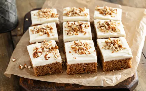 Nio bitar saftig morotskaka i långpanna med krämig frosting och hackade nötter, redo att avnjutas.