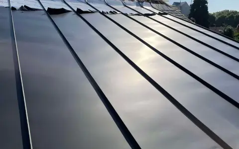Pose de feuilles de toit en zinc sur une nouvelle construction. Le soleil brille sur le métal lisse.